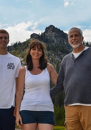 A woman and man standing with a young man in front of a mountain.