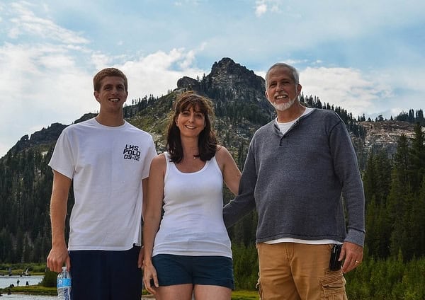 A woman and man standing with a young man in front of a mountain.