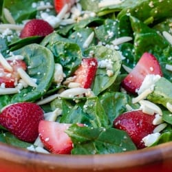 A close up of Strawberry Spinach Salad in a wooden salad bowl on a red cloth.