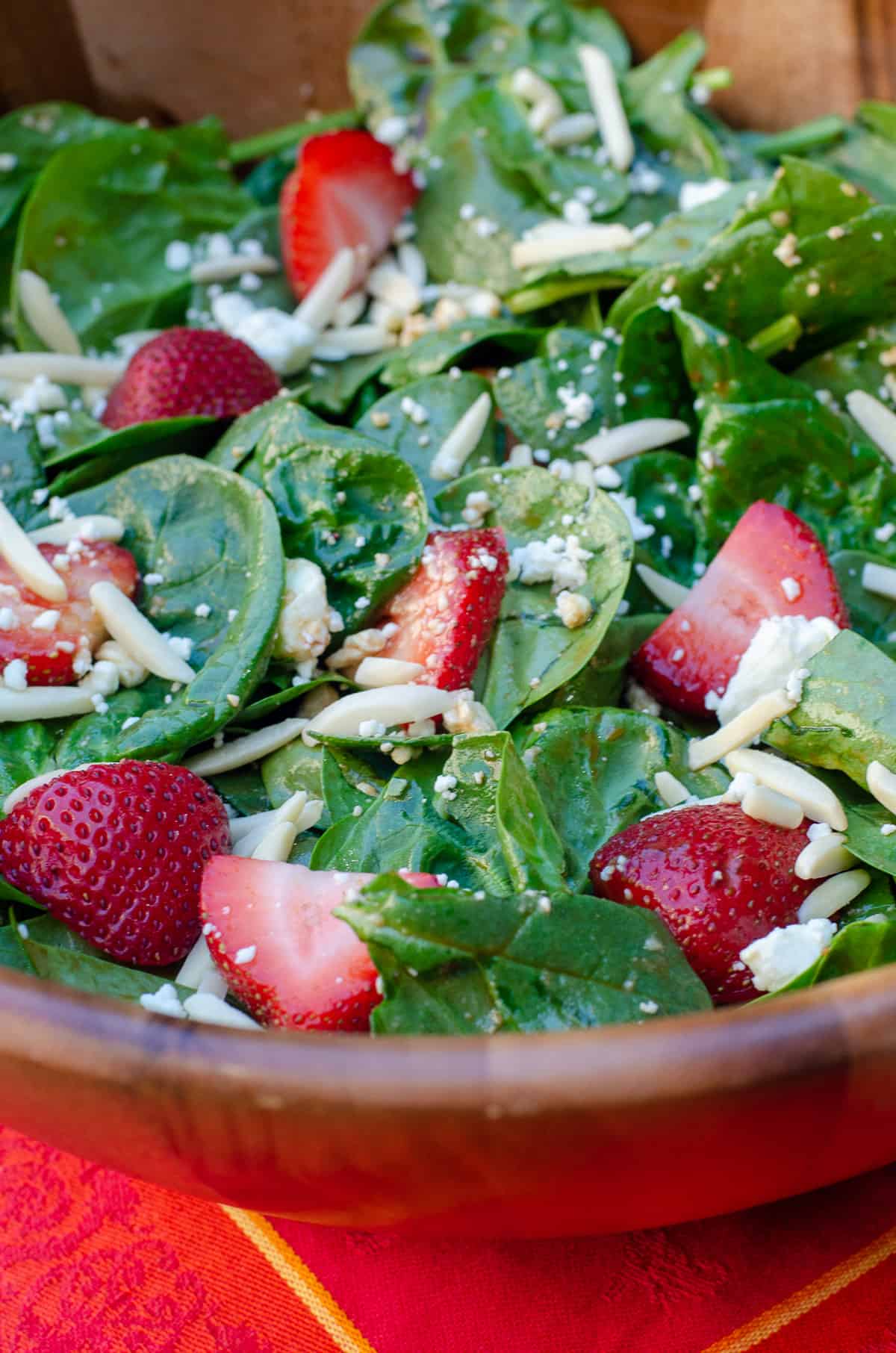 A close up of Strawberry Spinach Salad in a wooden salad bowl on a red cloth.