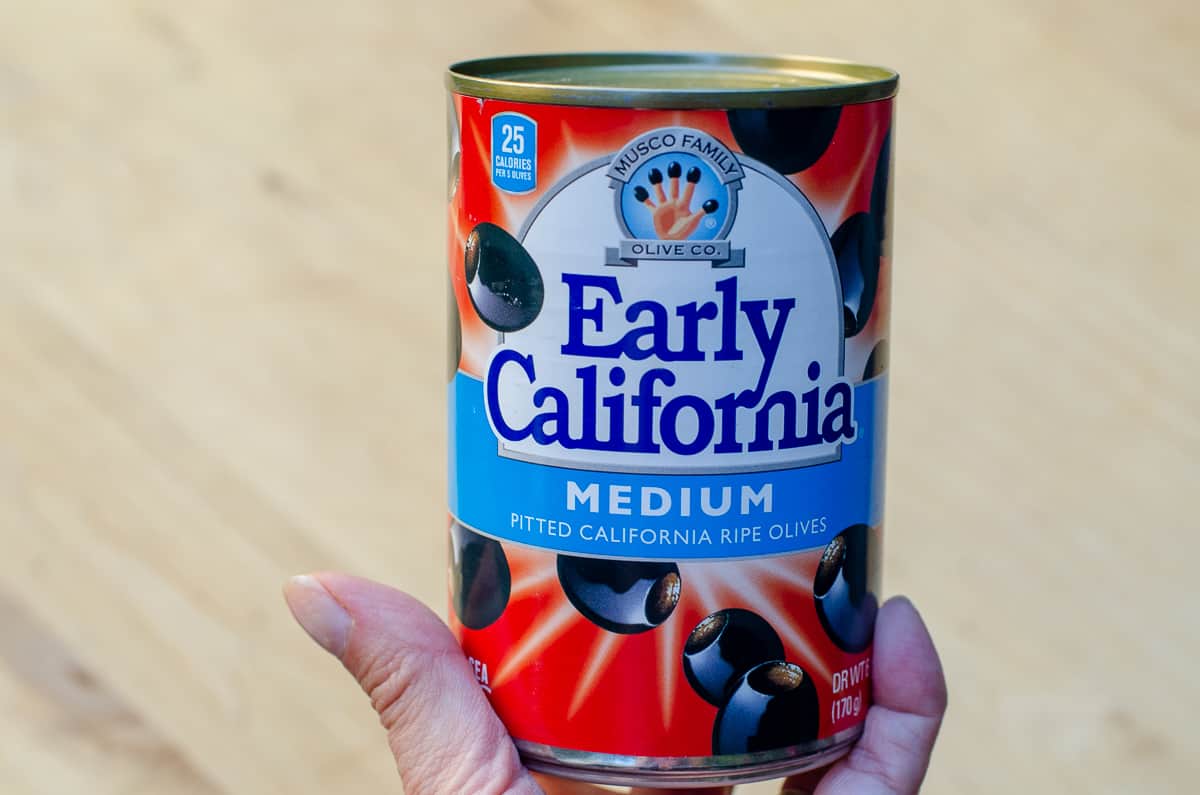 A hand holding a can of Early California black olives.