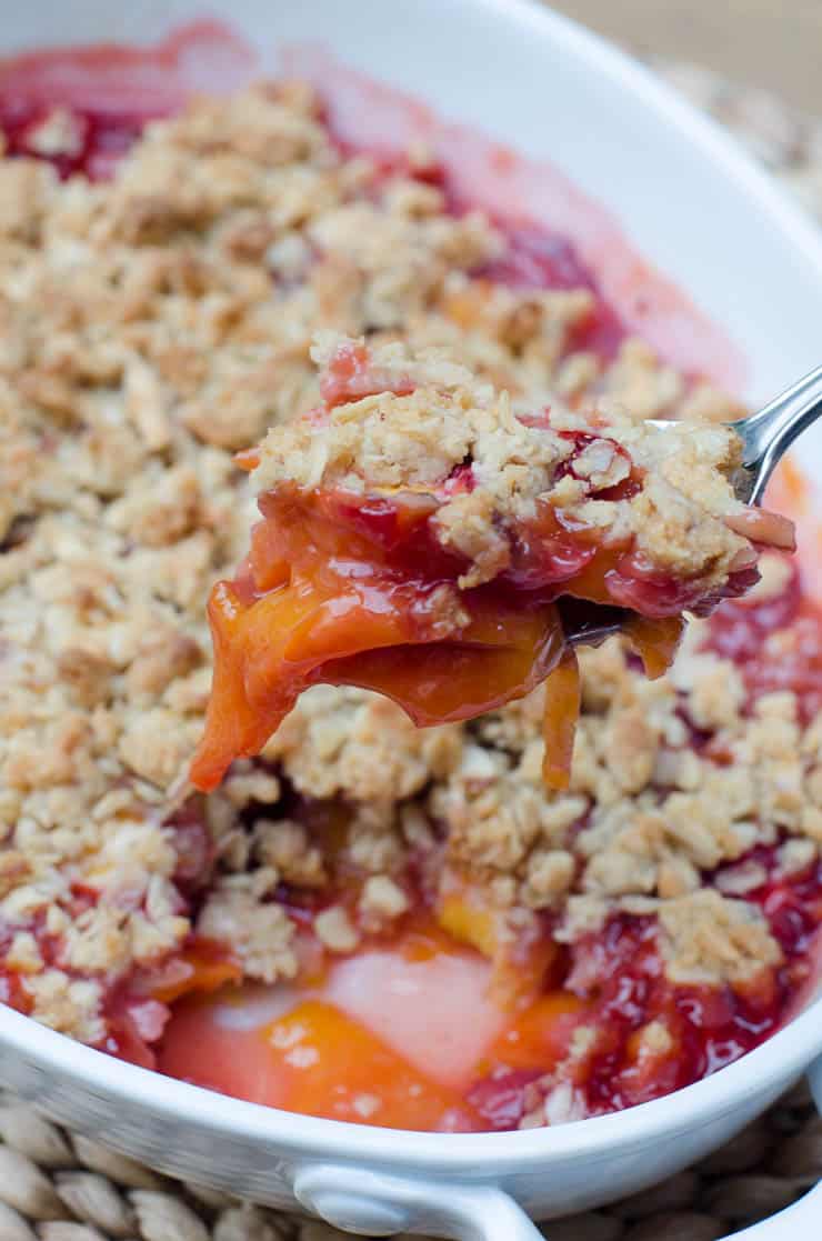 A spoon scoops up some Peach Strawberry Crisp from the baking dish.