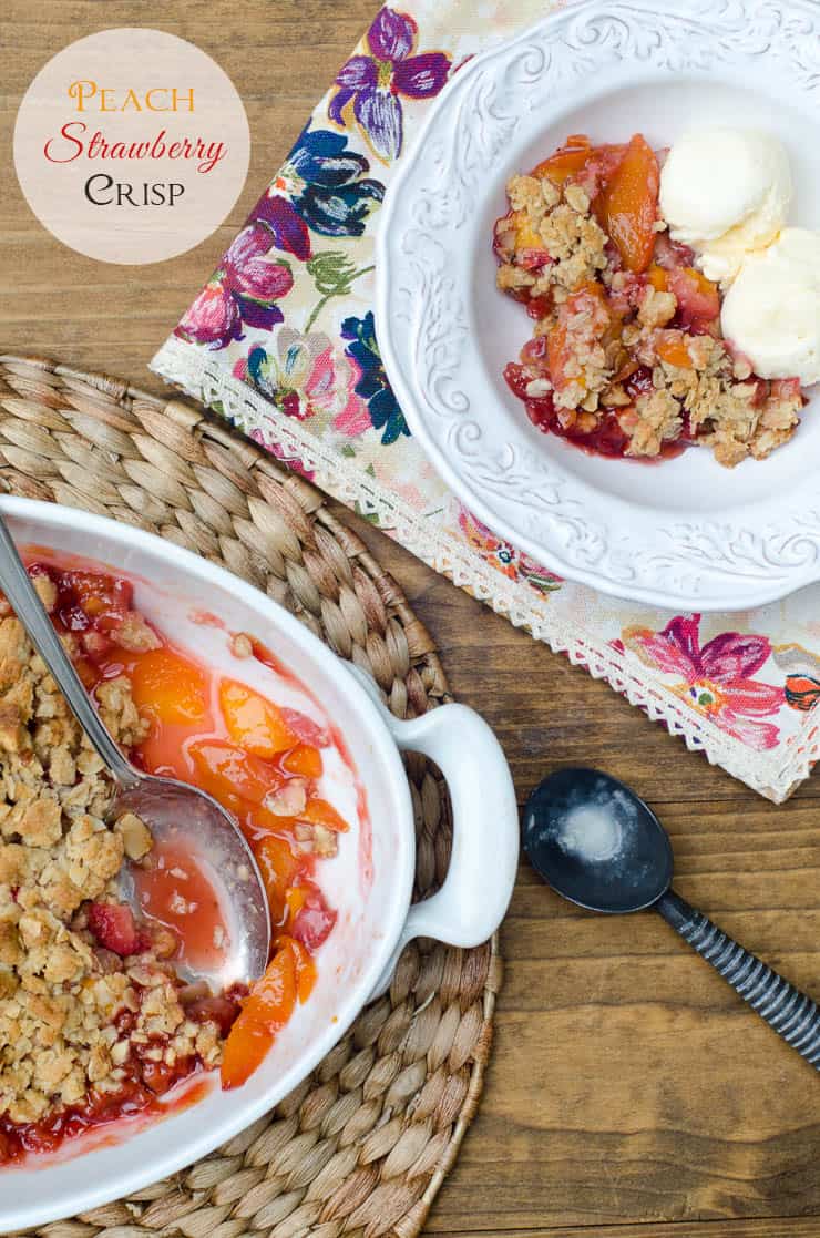 An over the top shot of Peach Strawberry Crisp in a white baking dish and small white bowl with ice cream with text overlay.