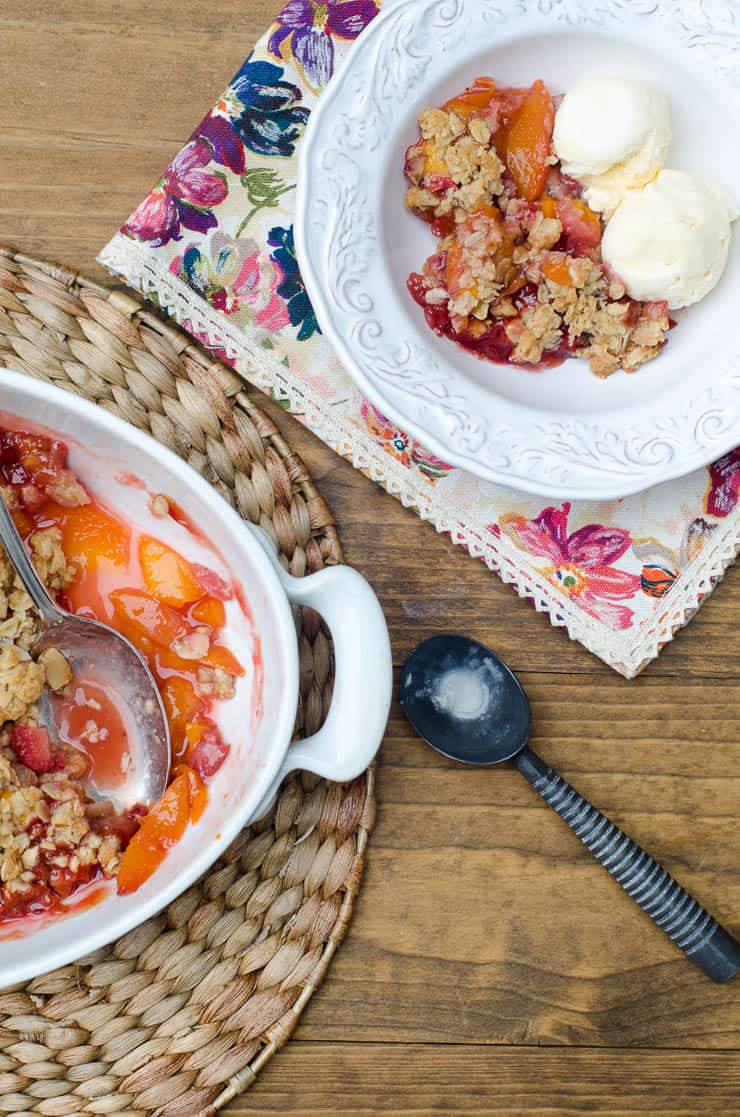 Peach Strawberry Crisp in a white baking dish and small white bowl with ice cream shot from over the top.