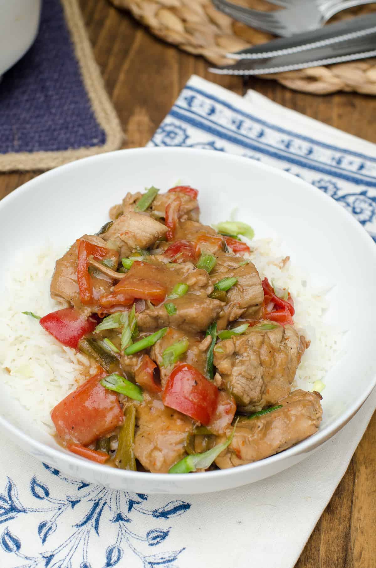 Cooked pork with red bell pepper on rice in a white bowl.