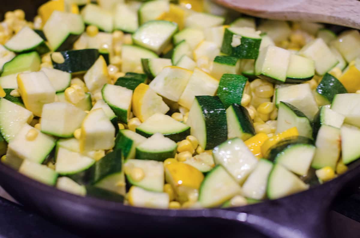 Green and yellow zucchini cooking in a skillet.