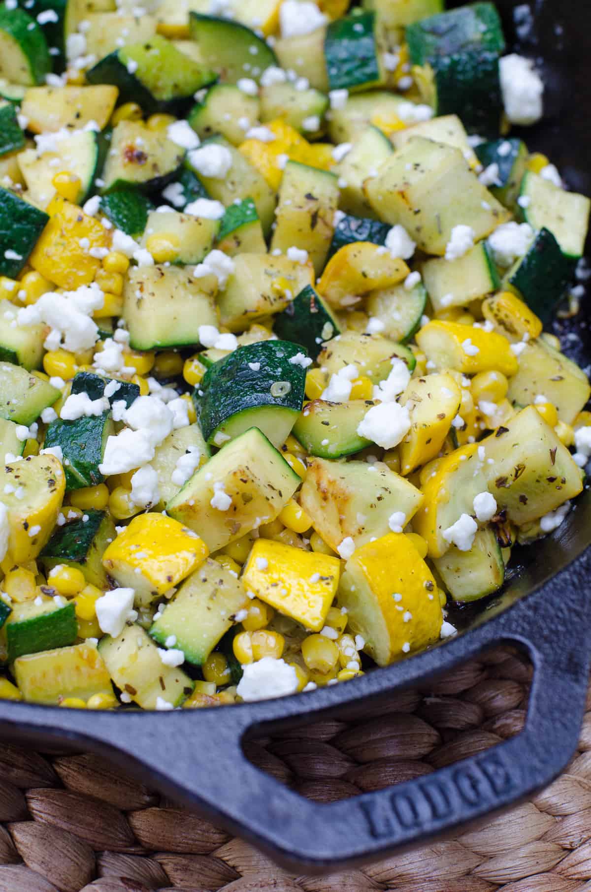 A close up of zucchini with corn and feta in a cast iron skillet.