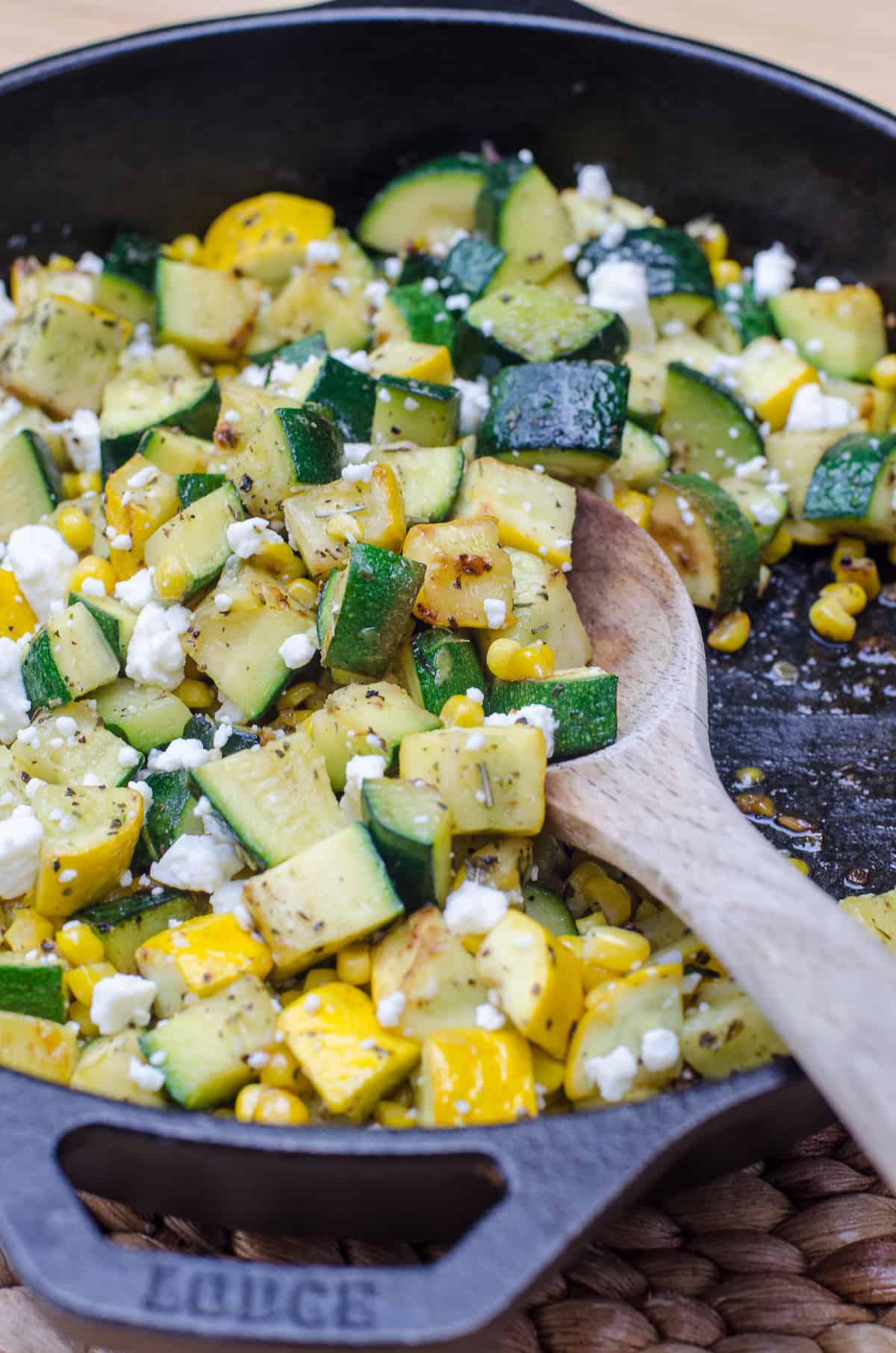 A close up of a wooden spoon scooping zucchini and corn from a skillet.