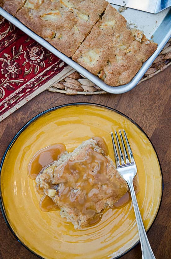 A slice of Apple Cake smothered in Butterscotch Sauce on a yellow plate with a fork.