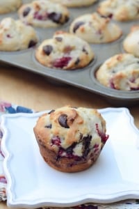 A muffin with raspberries and dark chocolate chips on a white plate.