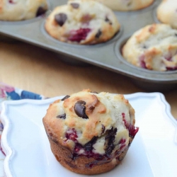 A muffin with raspberries and dark chocolate chips on a white plate.
