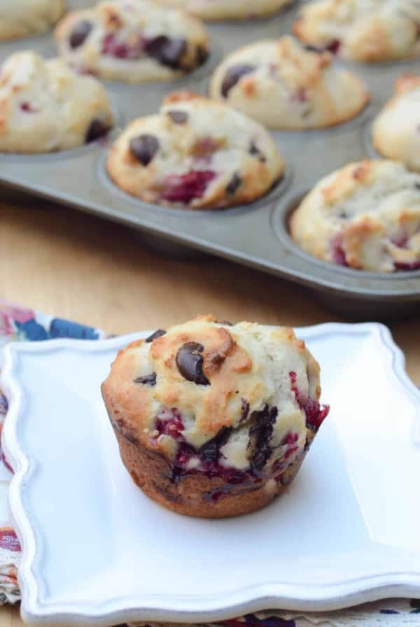 A muffin with raspberries and dark chocolate chips on a white plate.