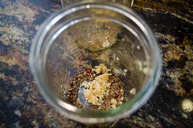 The pickling spices and garlic are added to a mason jar.