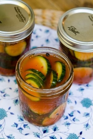 A mason jar filled with pickles in a reddish brine.