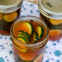 A mason jar filled with pickles in a reddish brine.