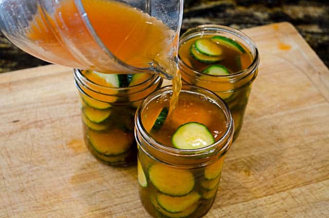 The brining liquid is poured into the mason jars full of sliced cucumbers.