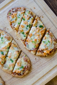 A slice of pizza sitting on top of a wooden cutting board, with Chicken and Flatbread