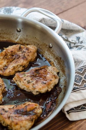 Chicken cooks in sauce in a skillet.