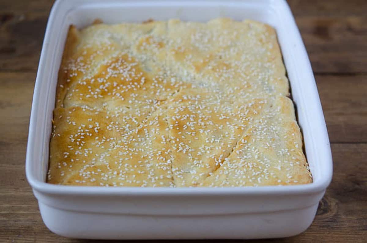 A casserole with a golden brown crescent roll top with sesame seeds in a white baking dish.