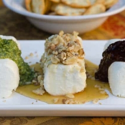 Logs of goat cheese with toppings on a white platter.