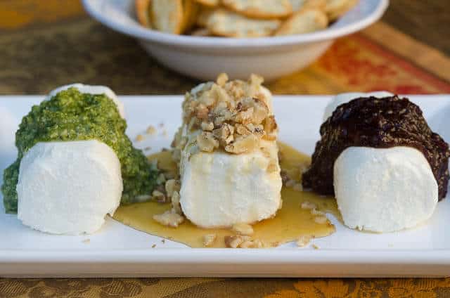 Logs of goat cheese with toppings on a white platter.