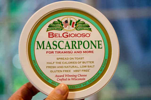 A hand holds a container of Belgioioso Mascarpone.