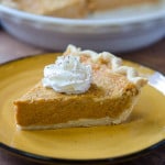 A piece of pumpkin pie topped with whipped cream on a yellow plate.