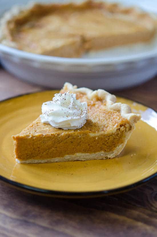 A slice of Pumpkin Hazelnut Pie with Mascarpone topped with whipped cream on a gold plate.