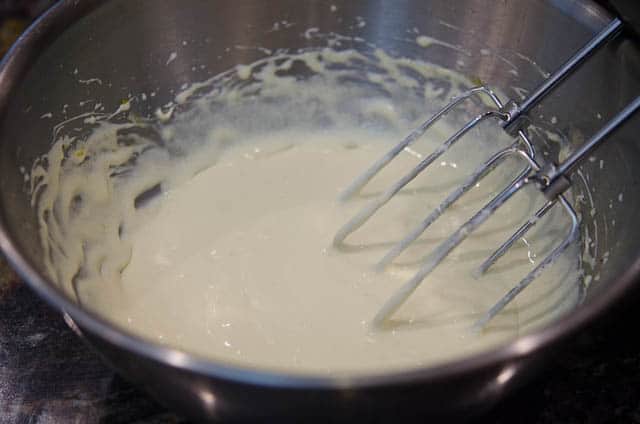Beaters whipping cream in a metal bowl.