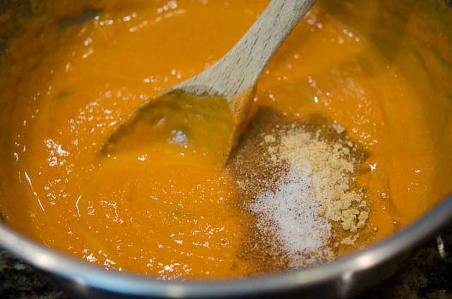 A wooden spoon mixing spices into pumpkin puree in a metal bowl.
