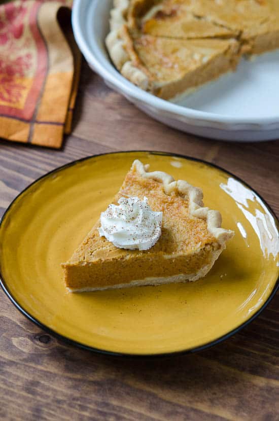 A slice of pumpkin pie topped with whipped cream on a gold plate.