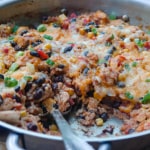 A spoon scoops into a skillet full of Tex-Mex Chicken and Rice
