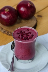 A red smoothie topped with pomegranate seeds in a glass.