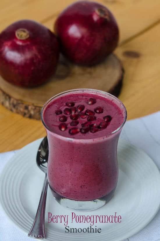 A red smoothie topped with pomegranate seeds in a glass.