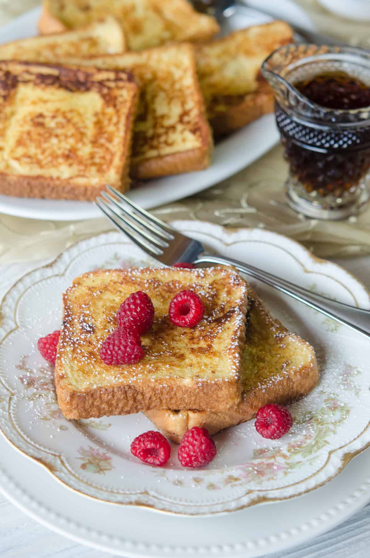 Two slices of eggnog french toast topped with powdered sugars on a china plate with raspberries.