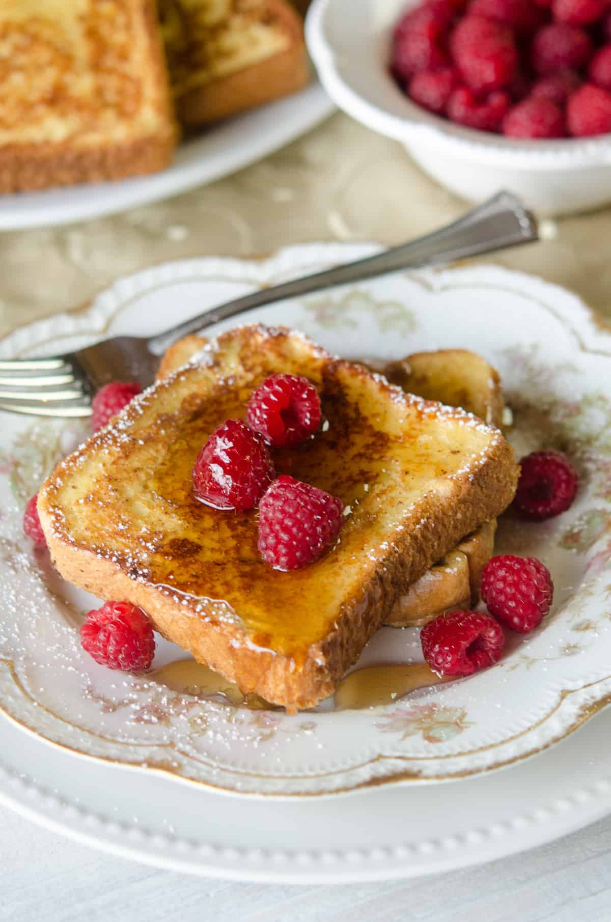 French toast made with eggnog topped with syrup on a china plate with raspberries.