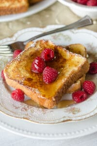 French toast made with eggnog topped with syrup on a china plate with raspberries.
