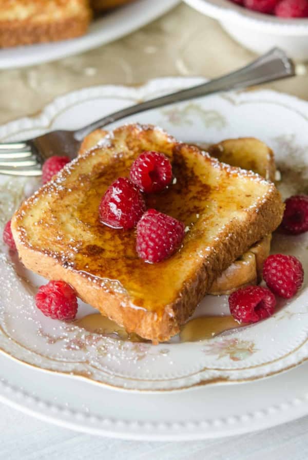French toast made with eggnog topped with syrup on a china plate with raspberries.