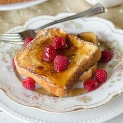 French toast with syrup and raspberries on a pretty china plate.