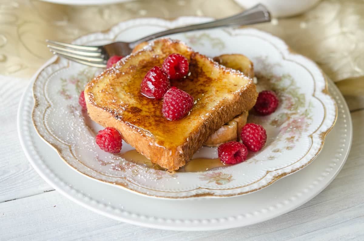 French toast made with eggnog topped with syrup on a china plate with raspberries.