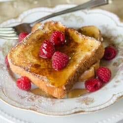 French toast made with eggnog topped with syrup on a china plate with raspberries.