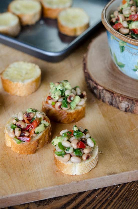 White Bean, Black-Eyed Pea, Avocado Crostini on a wooden cutting board.