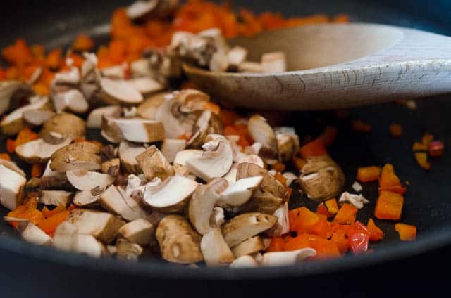 Diced red bell pepper and mushrooms cooking in a skillet.