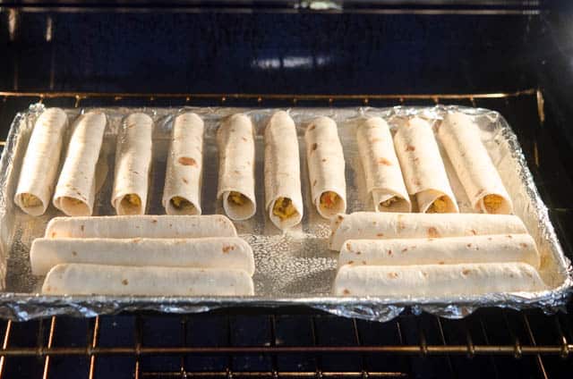 Crispy Baked Breakfast Taquitos in the oven on a foil lined baking sheet.
