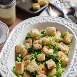 Caesar salad with shrimp and croutons in a white bowl.