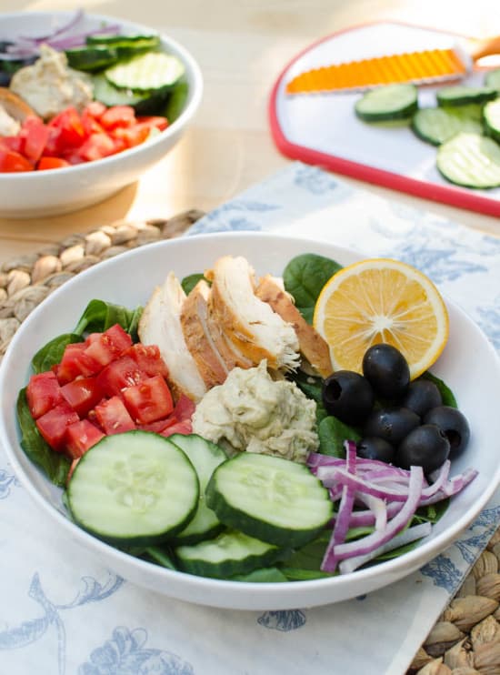 A bowl filled with spinach, veggies, chicken and hummus.