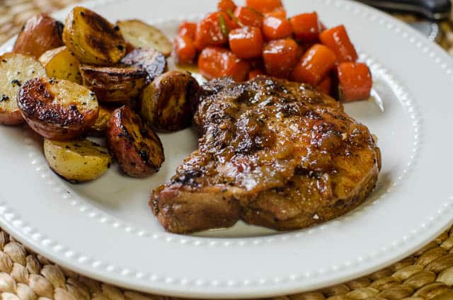 Una chuleta de cerdo en un plato blanco con zanahorias y patatas.