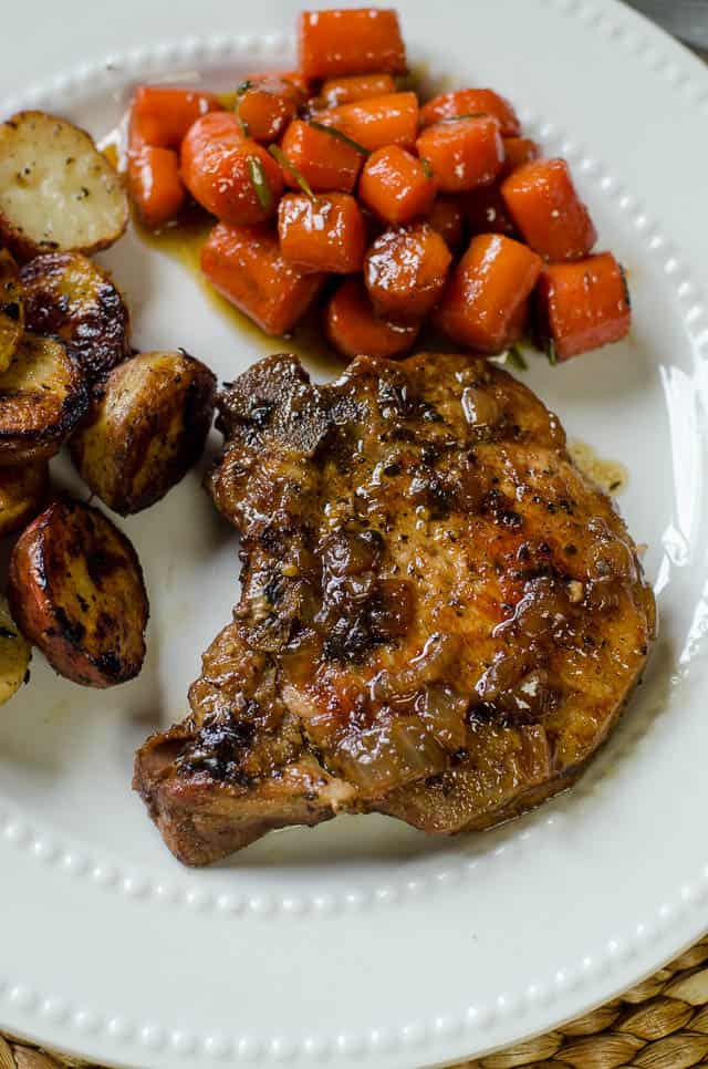 Skillet Braised Pork Chops on a white plate with carrots and potatoes.