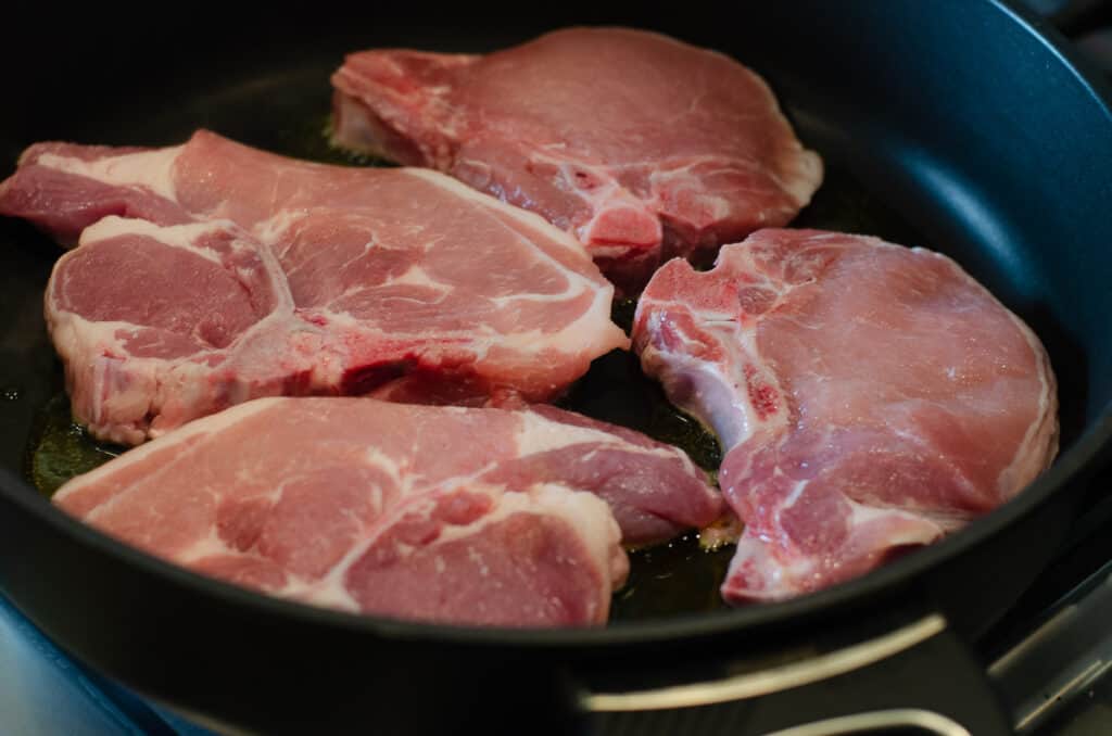 Pork chops cooking in a skillet.