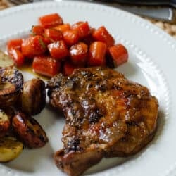A pork chop on a white plate with carrots and potatoes.